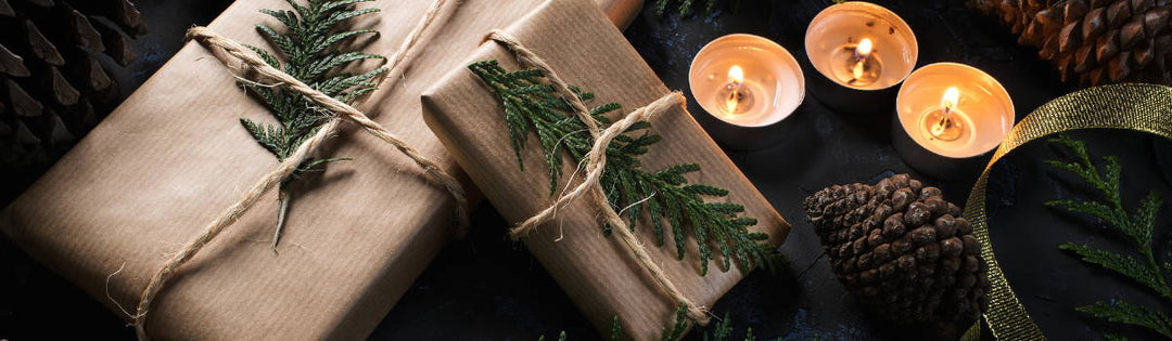 Zwei Weihnachtgeschenke in brauenm Papier mit Tannenzweigen und drei Teelichtern.