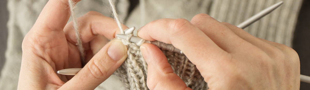 Zwei Hände stricken mit beigem Garn.