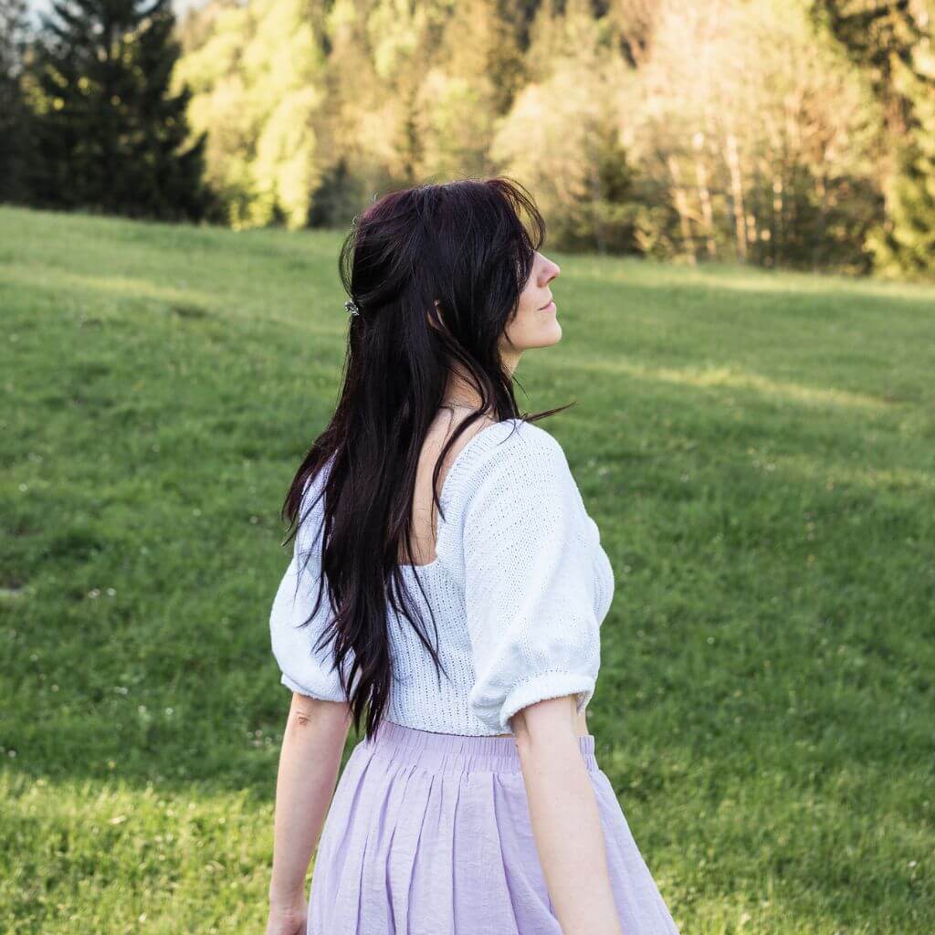 A woman with long hair walks through a green field.
