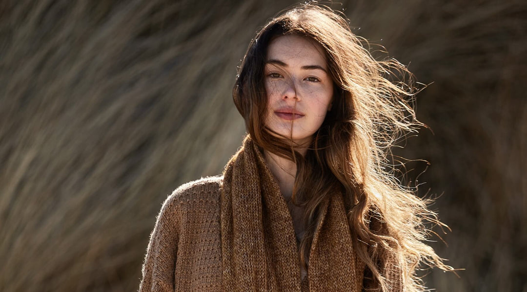 A woman with long hair wearing a brown scarf in a natural setting.