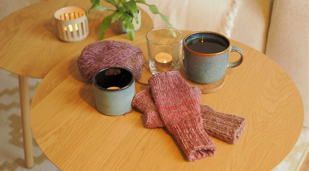 Gestrickte Stulpen, eine Tasse  sowie eine Pflanze auf einem Holztisch.